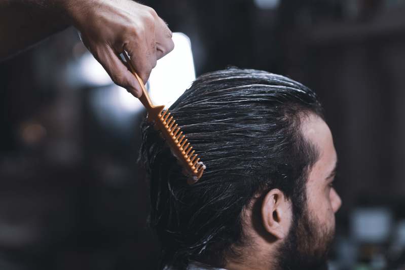 Close-up of various hair pomade jars and styling tools on a marble surface