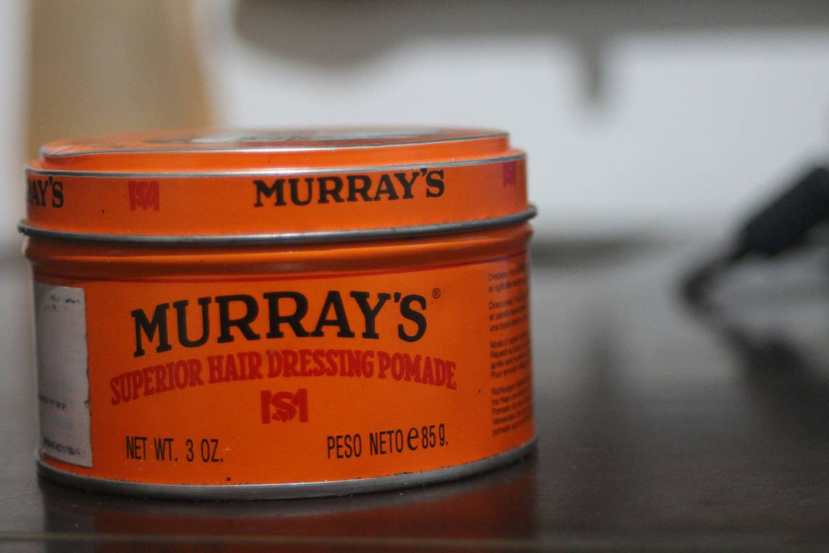 Hand scooping strong hold pomade from a tin jar for styling textured short hair